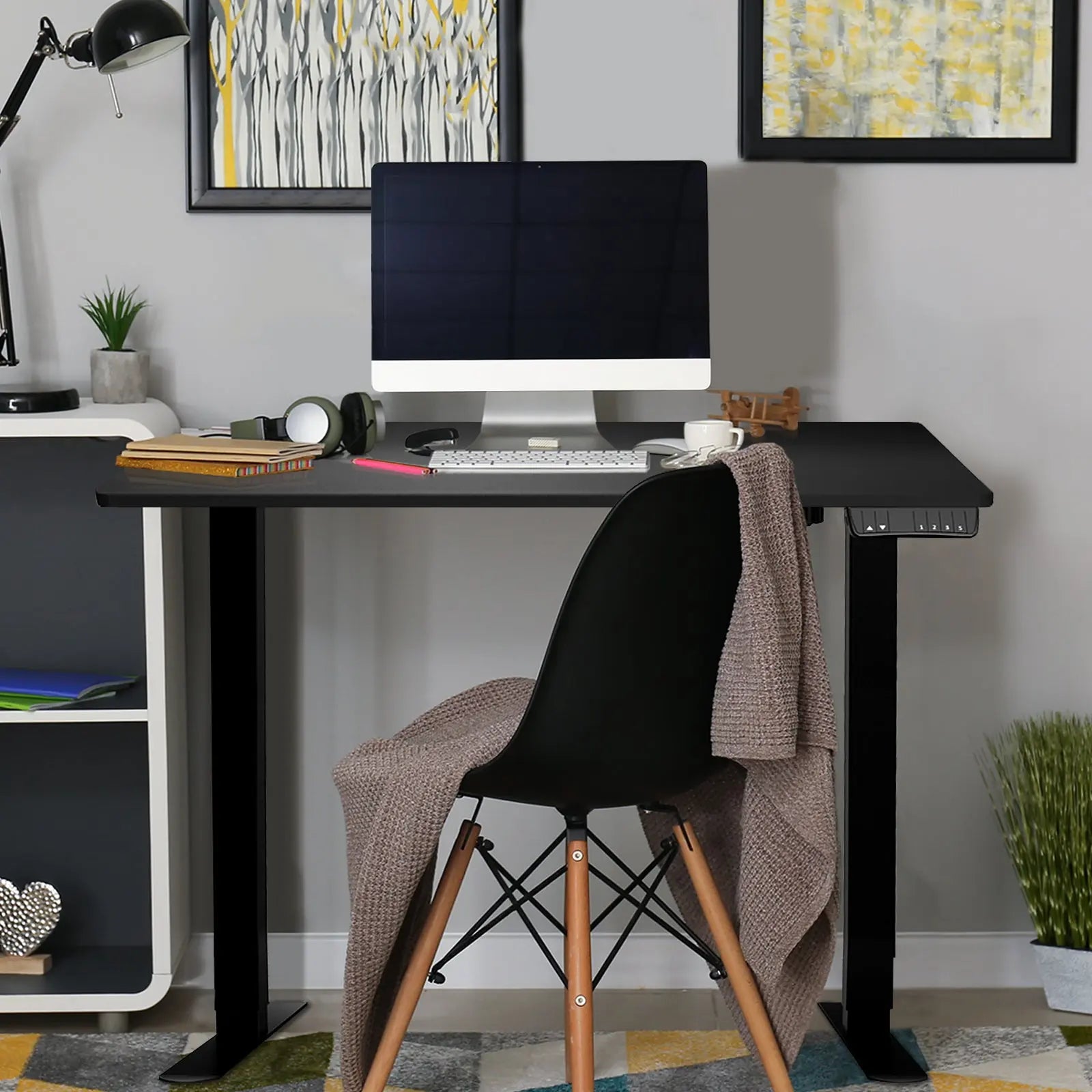 A stylish home office setup showcasing a black motorized desk with a desktop monitor, surrounded by modern decor and furniture.