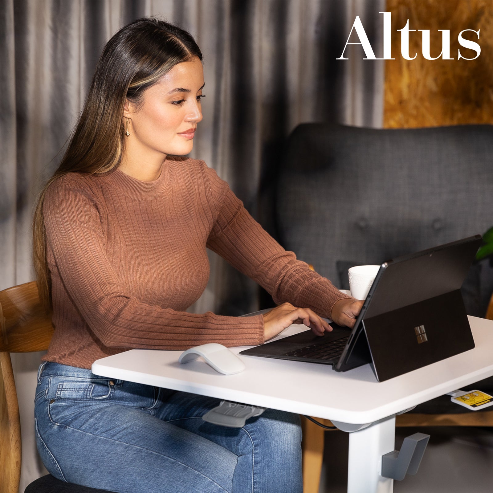 Woman in a casual brown sweater using the desk in a seated position, illustrating the desk’s functionality in a cozy setting.