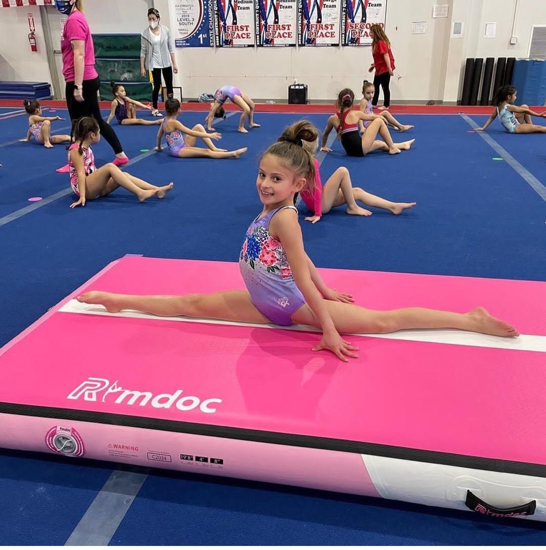 A little girl performing a split on the gymnastics mat.