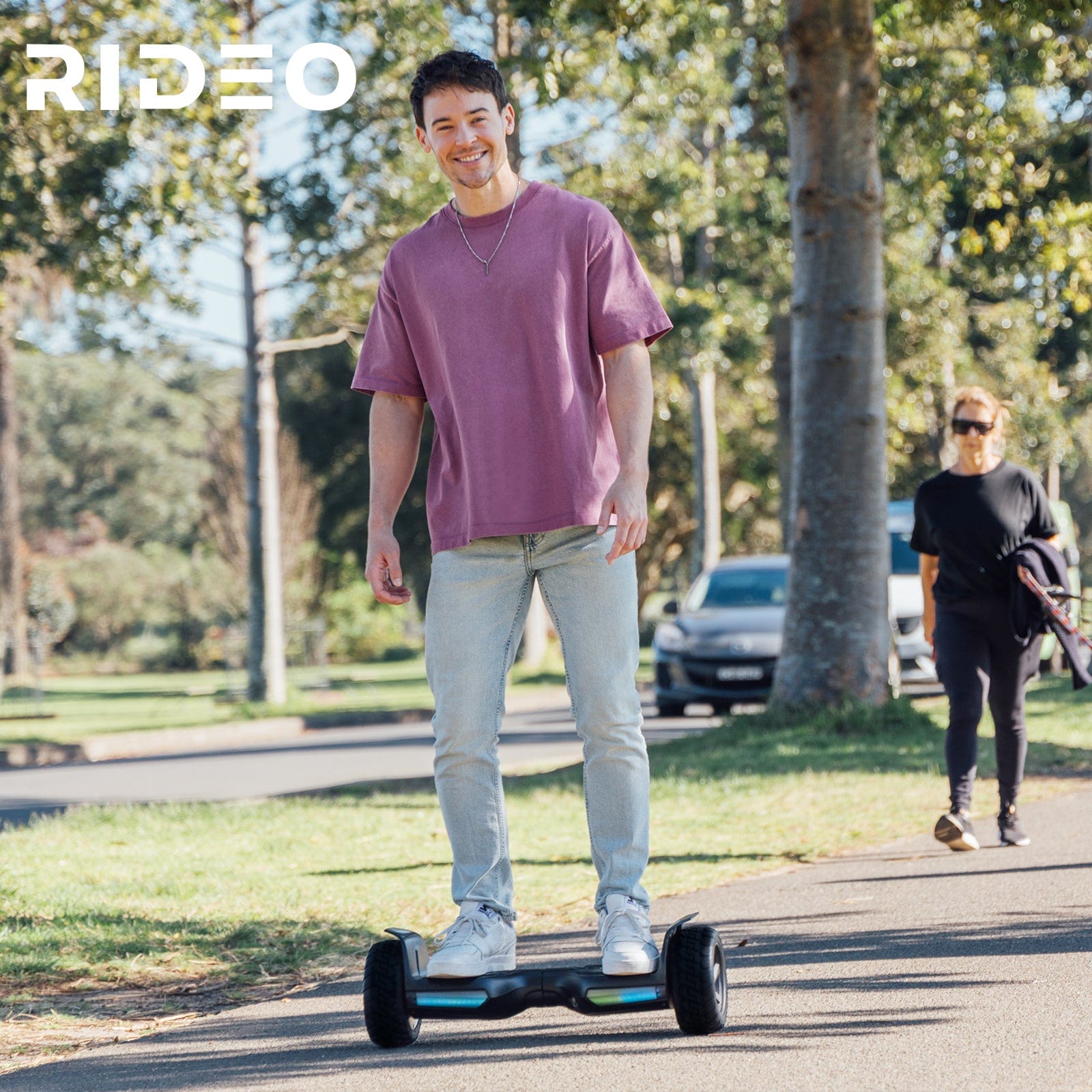 A young man enjoying a ride on a Rideo hoverboard in a sunny park, showcasing the hoverboard's stability and ease of use on outdoor paths.