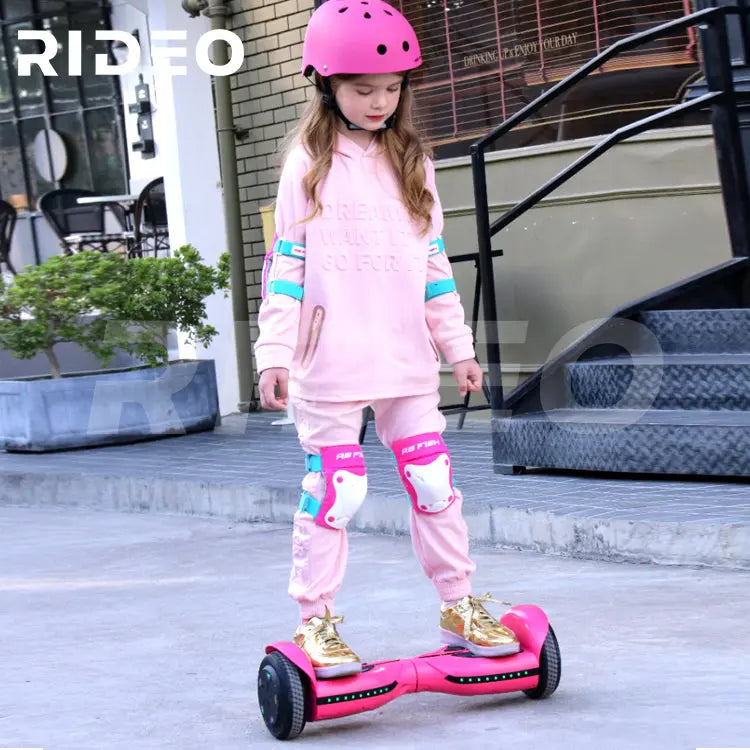 Young girl riding a pink RIDEO Q3c Self Balance Scooter, wearing pink safety gear and helmet, showcasing the hoverboard's design and smooth ride outdoors.