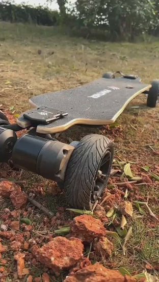 A skateboard starting up on an uneven, gravelly, and grassy terrain.